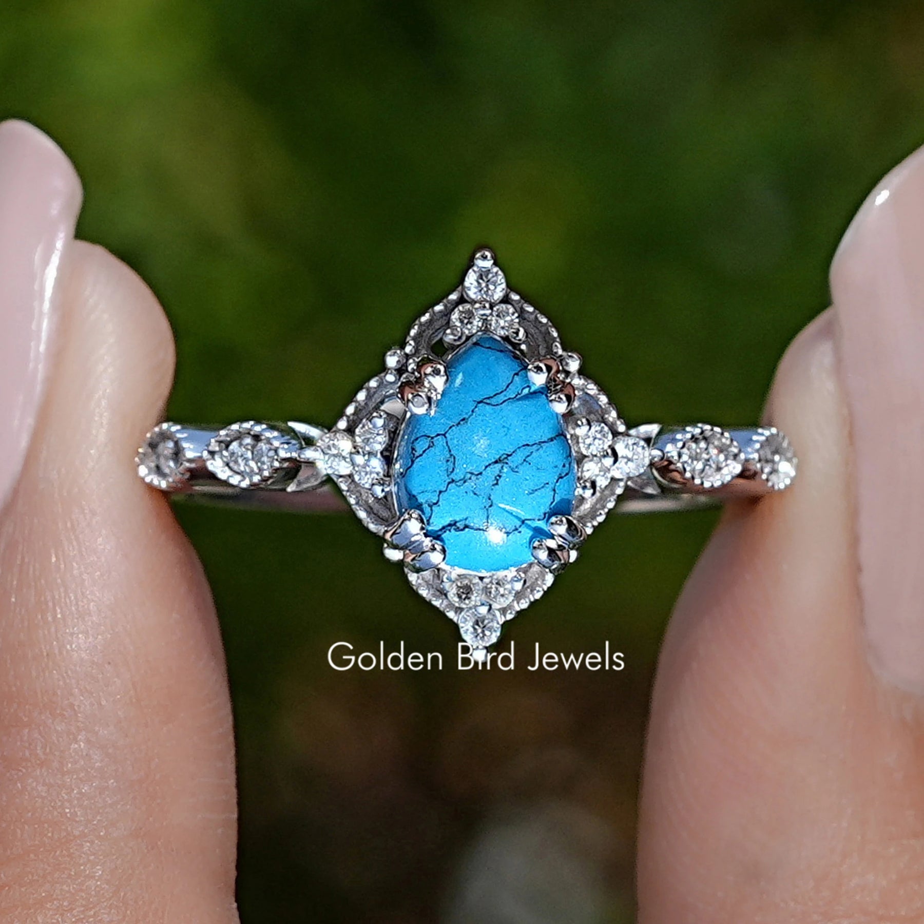 Front view of Blue Turquoise Pear Gemstone Accent Set Ring in two fingers