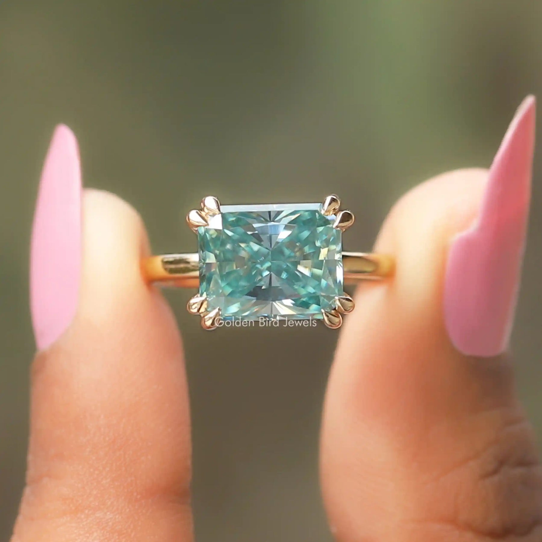 Two fingers holding the Blue Radiant Cut Moissanite Ring