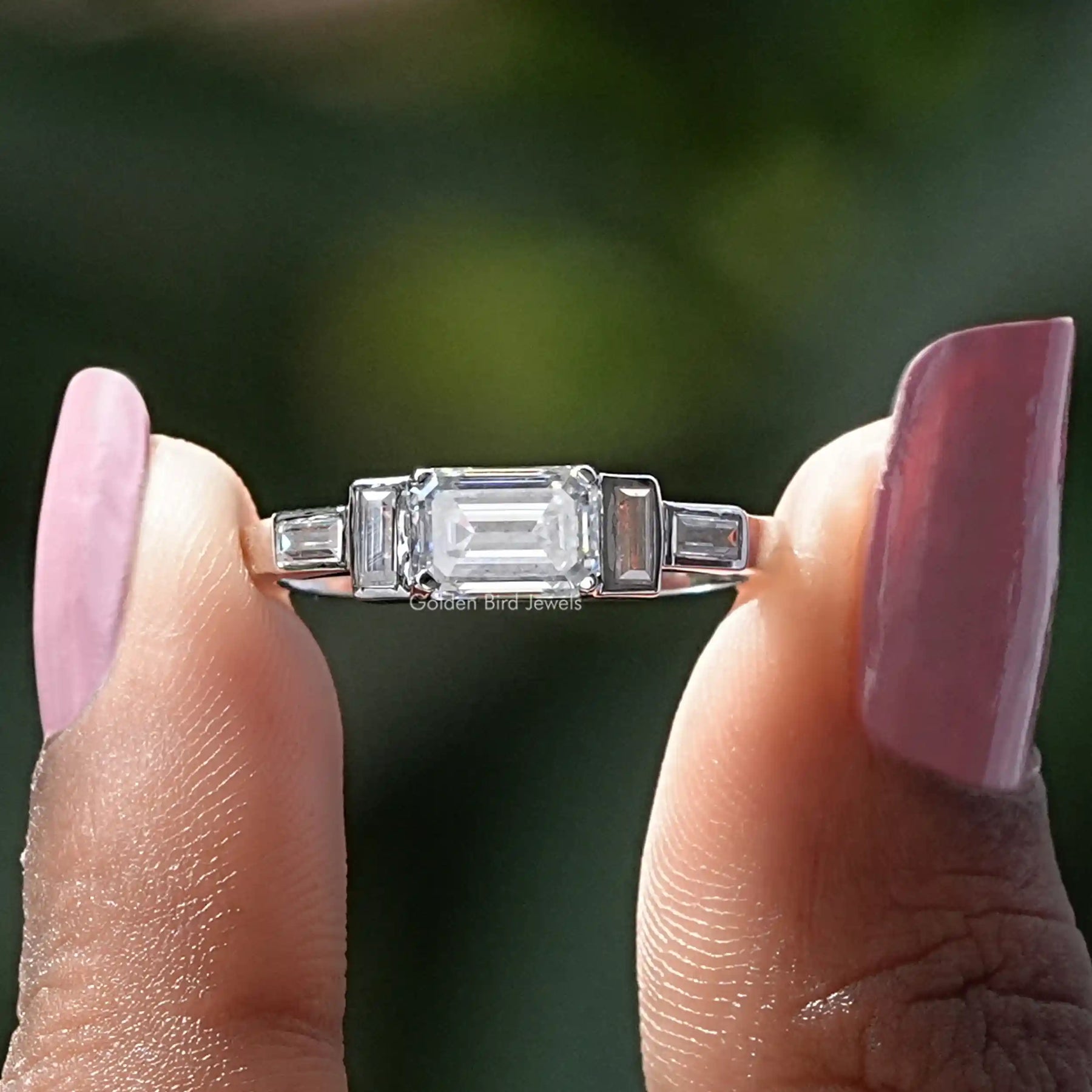 Two fingers holding the Emerald And Baguette Cut Moissanite Ring