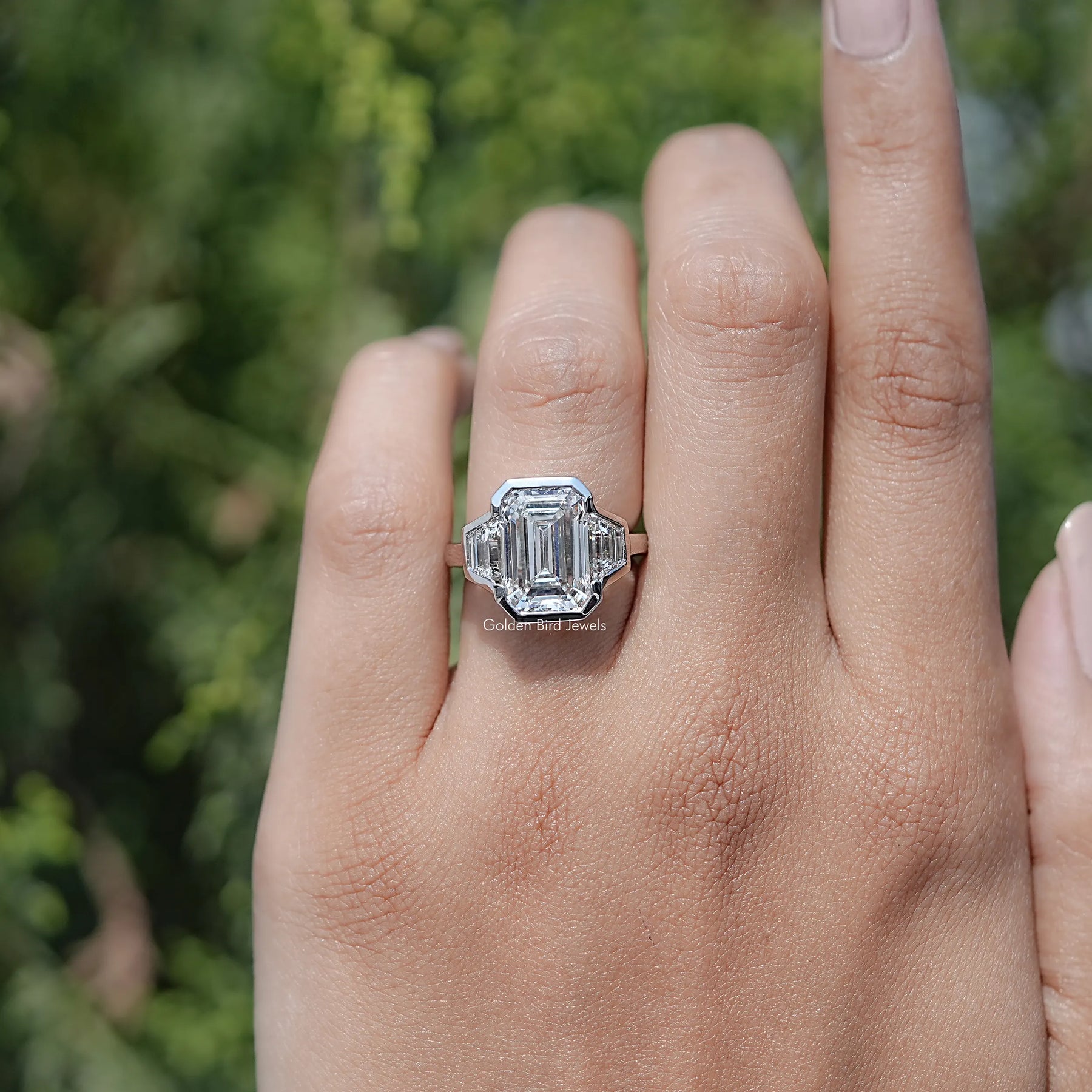 In finger view of Bezel Set Emerald Cut Lab Diamond Three Stone Ring