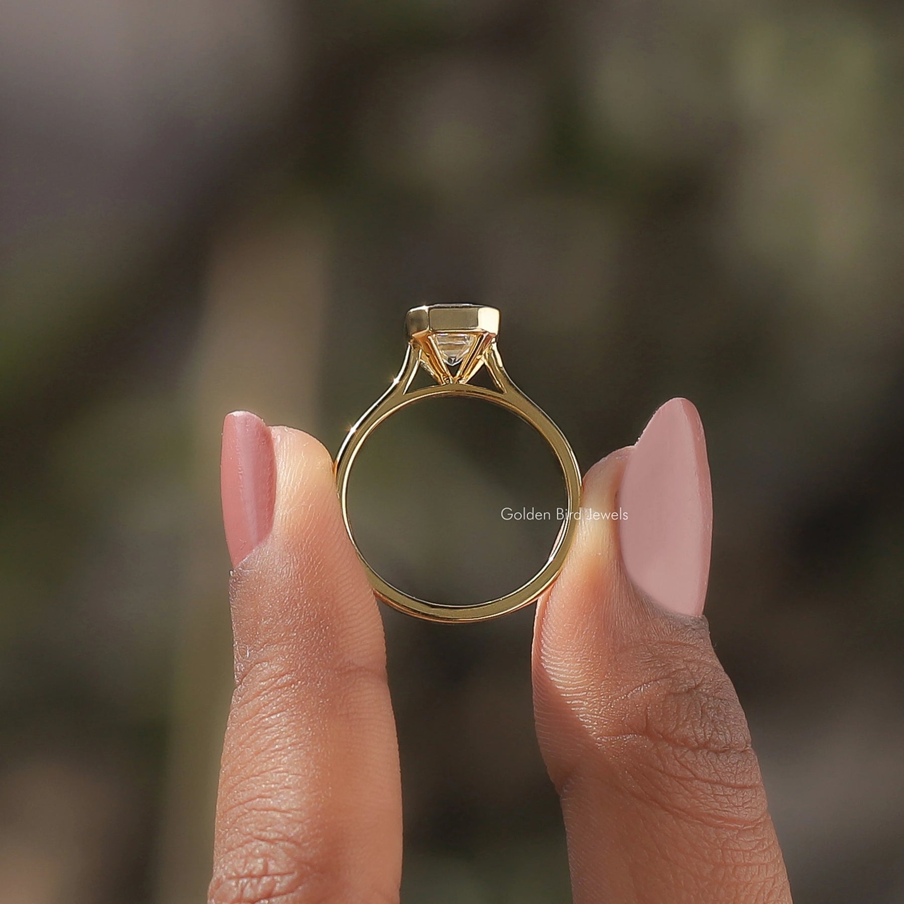 Back View of A Emerald Cut Bezel Set Moissanite Ring In two fingers
