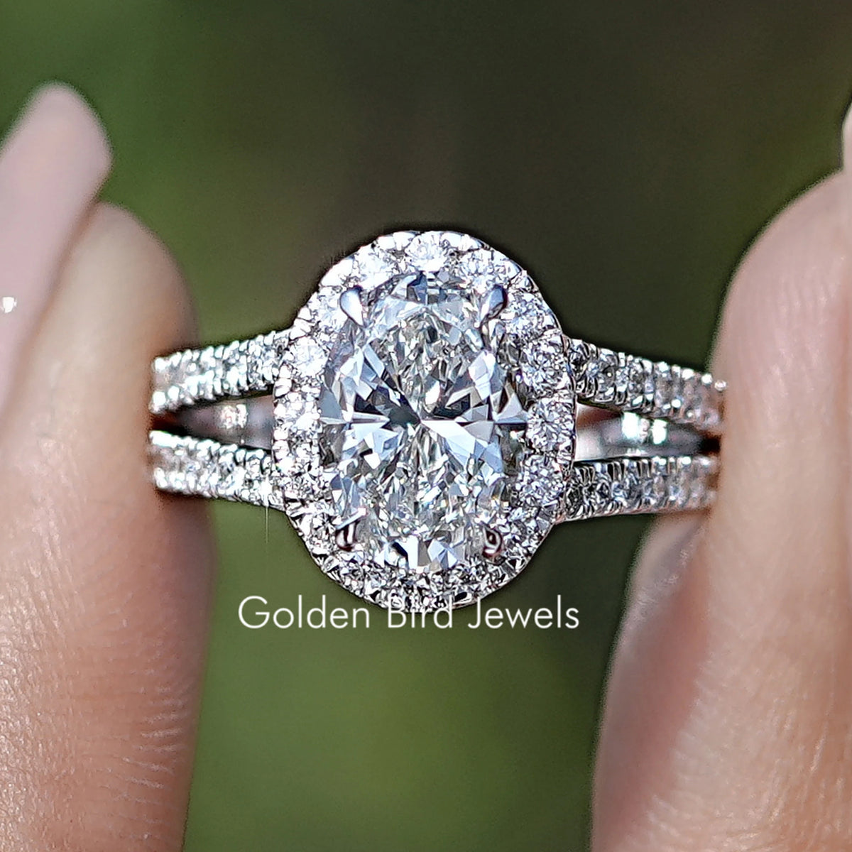 Oval Cut Halo Diamond Split Shank Engagement Ring Held Between Fingers