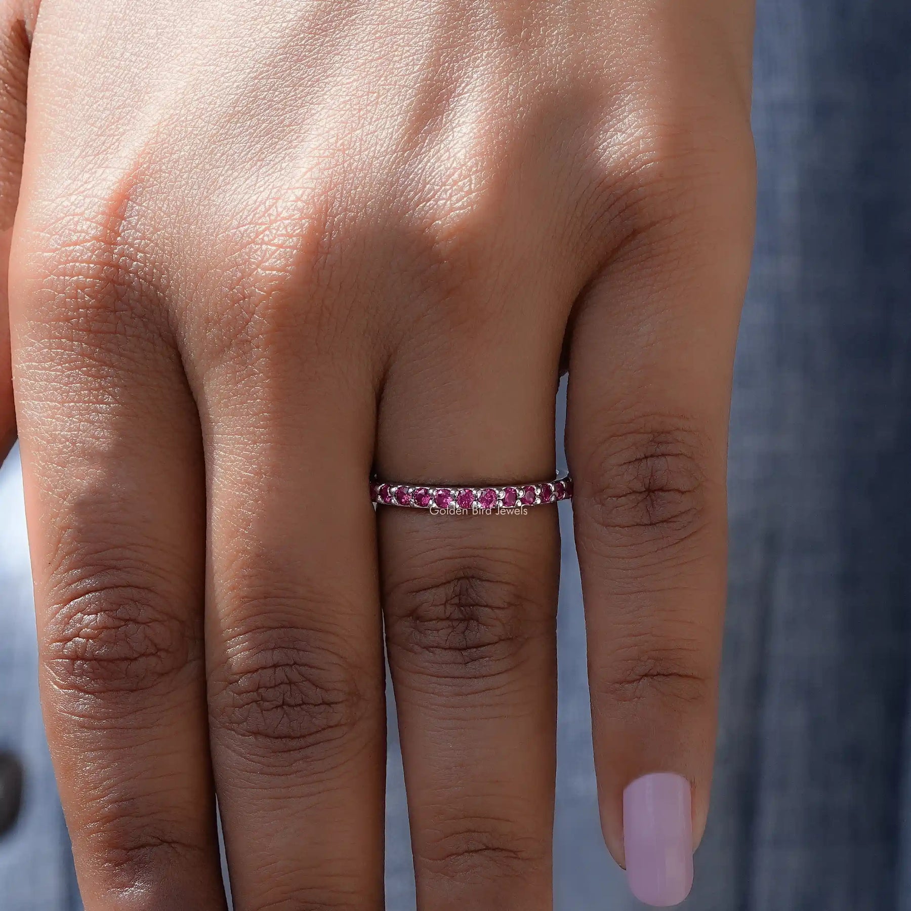 In finger front view of October Birthstone Pink Tourmaline Round Eternity Band in unique shape