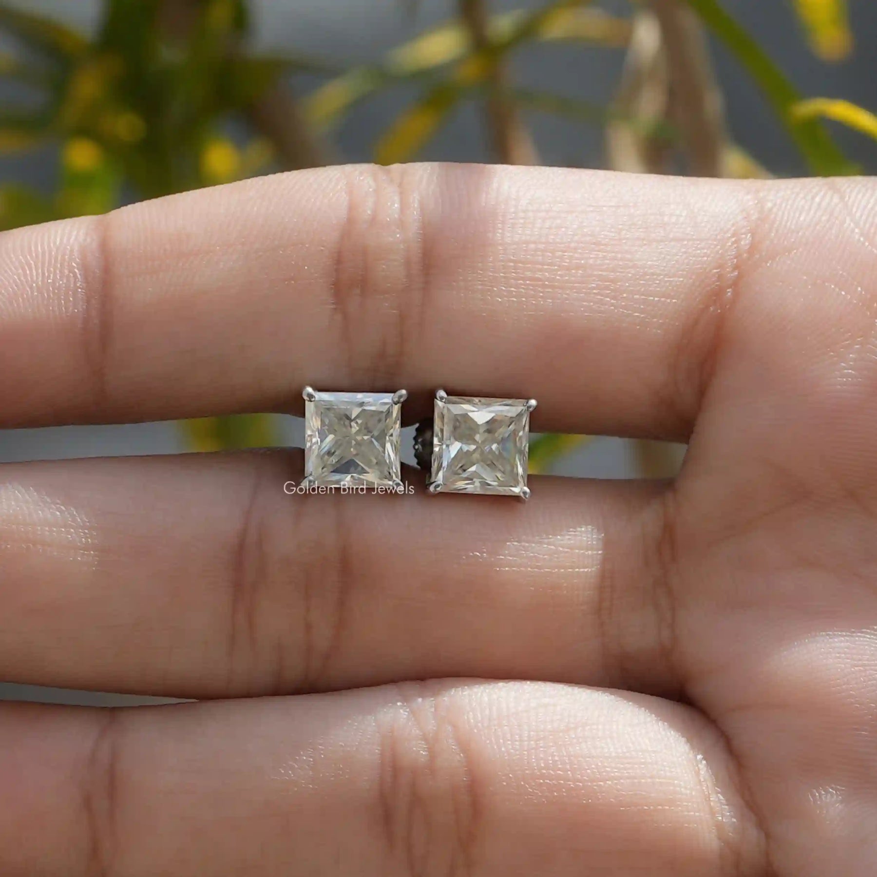 In two finger view of princess cut stud earrings