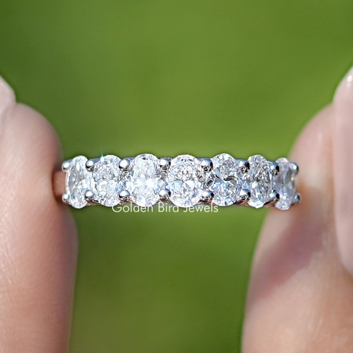 Lab Grown Diamond Oval Seven Stone Wedding Band Held Between Fingers