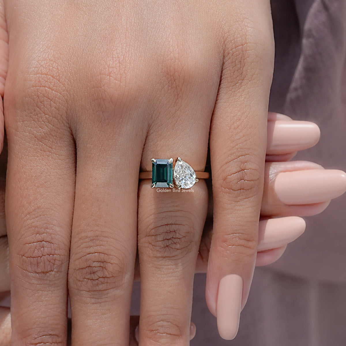 Two-stone ring with emerald-cut green stone and round white stone, worn on hand