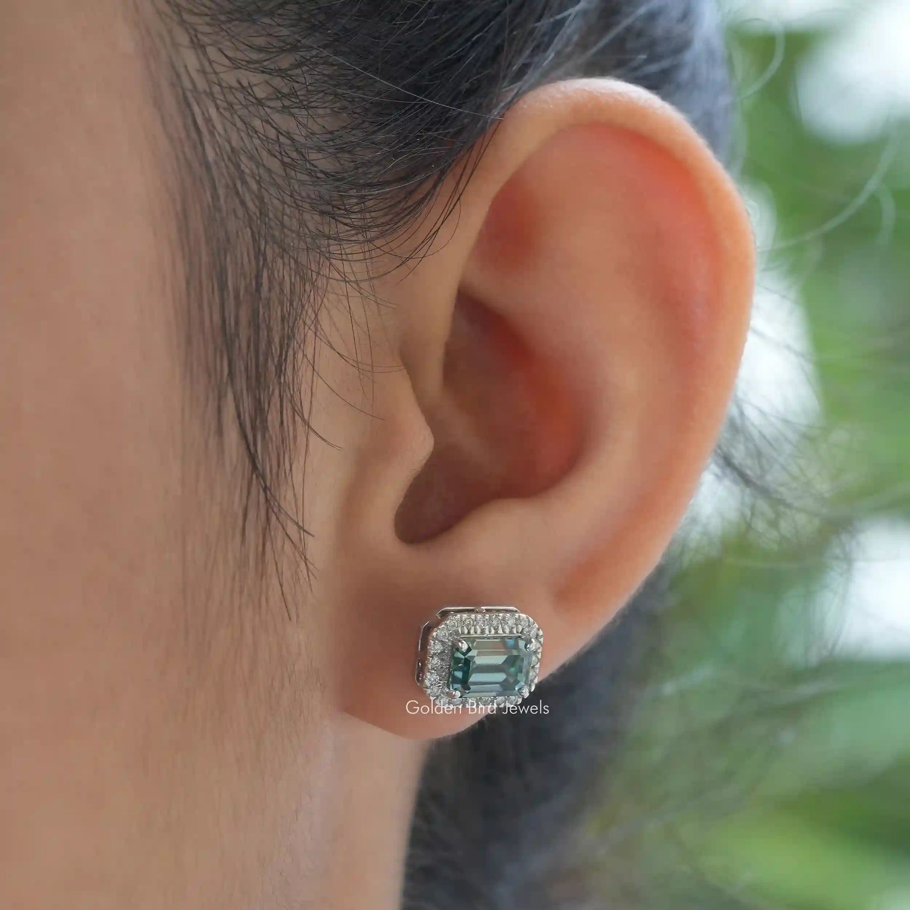 In ear front view of green emerald cut moissanite stud earrings in secure setting