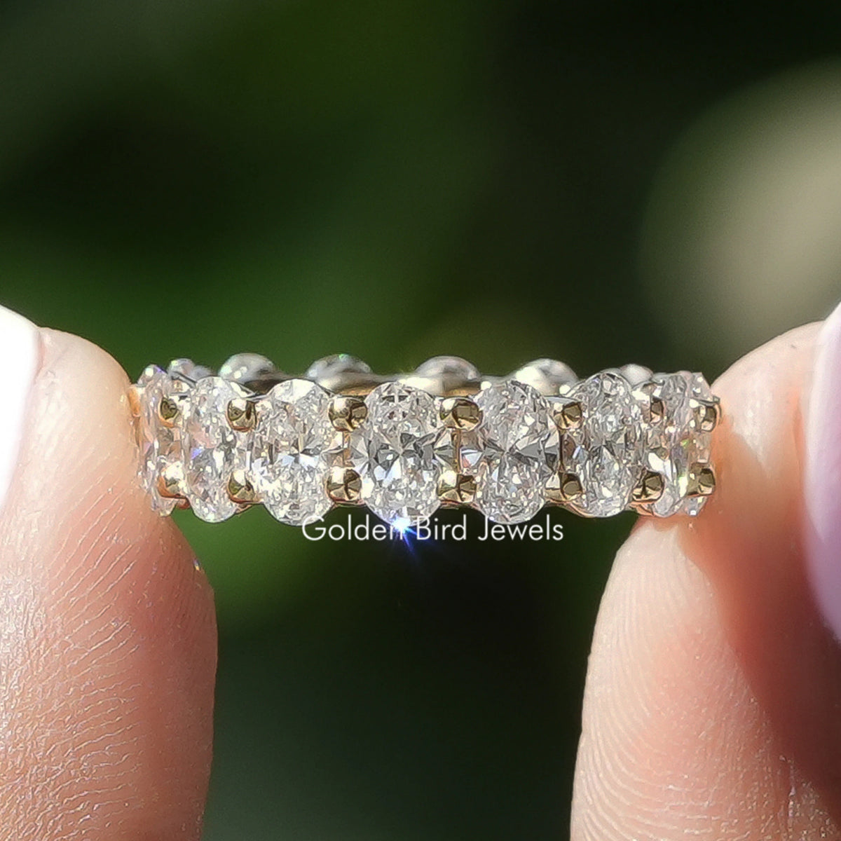 Oval Cut Lab Grown Diamond Eternity Band Held Between Fingers