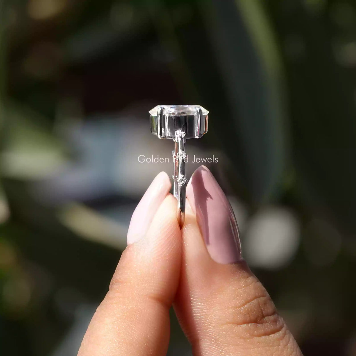 Side View of Oval Cut Accent Engagement Ring In two fingers