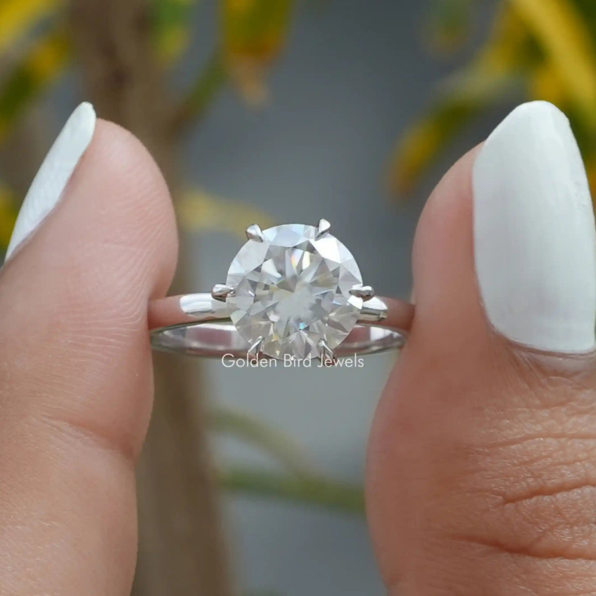 Round Cut Moissanite Engagement Ring held between two fingers