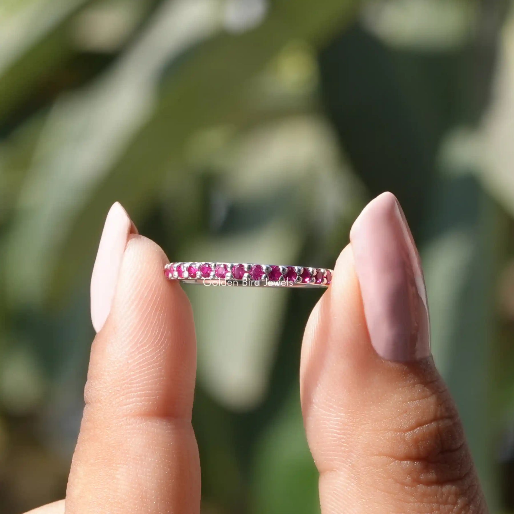 Two fingers holding the Round Shaped Ruby Gemstone Half Eternity Wedding Band