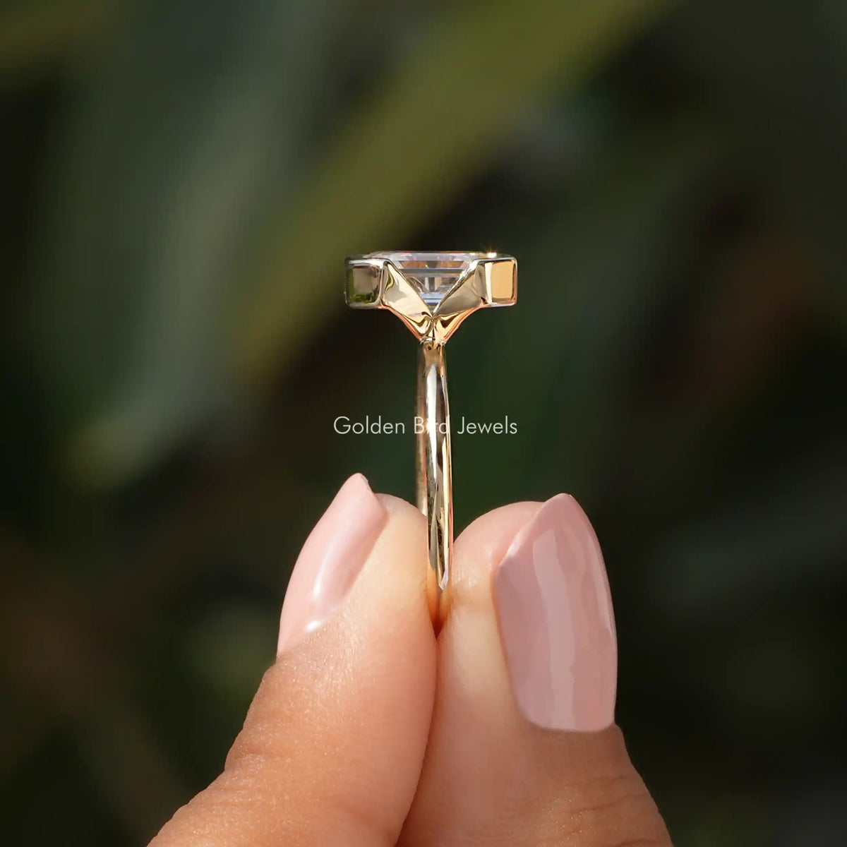 Side View of Emerald Cut Half Bezel Set Engagement Ring In two fingers