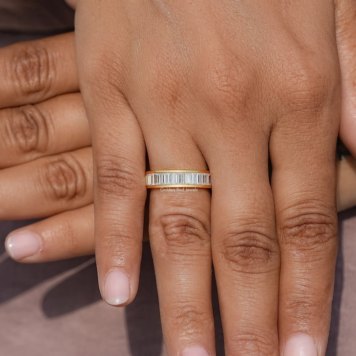 Yellow gold channel-set wedding band with baguette-cut moissanite, centered on hand