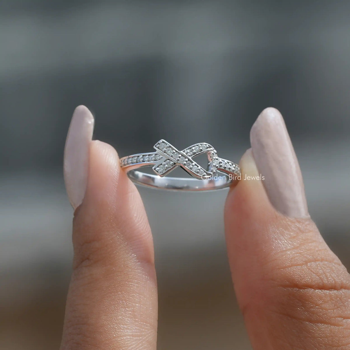 Two fingers holding the Ribbon Style Round Cut Moissanite Ring