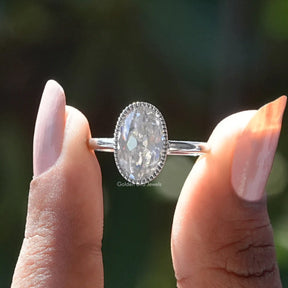 Two fingers holding the Oval Cut Bezel Set Moissanite Engagement Ring