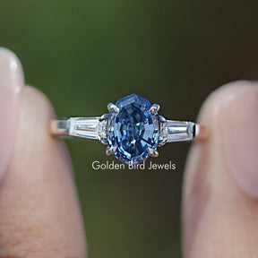 Front view of Blue Step Cut Oval Moissanite Three Stone Ring in two fingers 