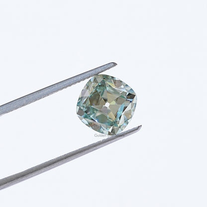 Light blue moissanite gemstone in silver tweezers, cushion old mine cut