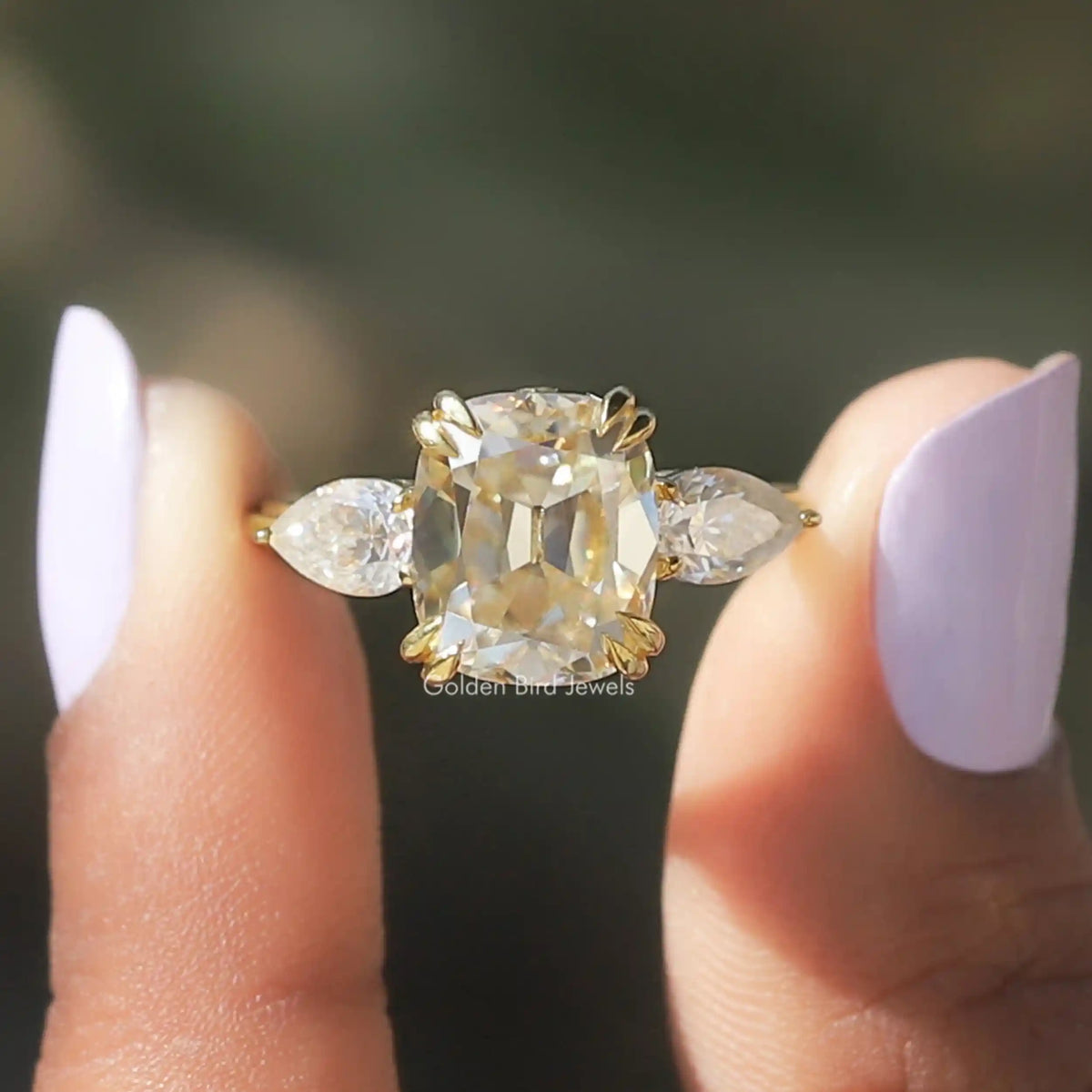 [In two finger front view of cushion and pear cut 3 stone moissanite ring]-[Golden Bird Jewels]
