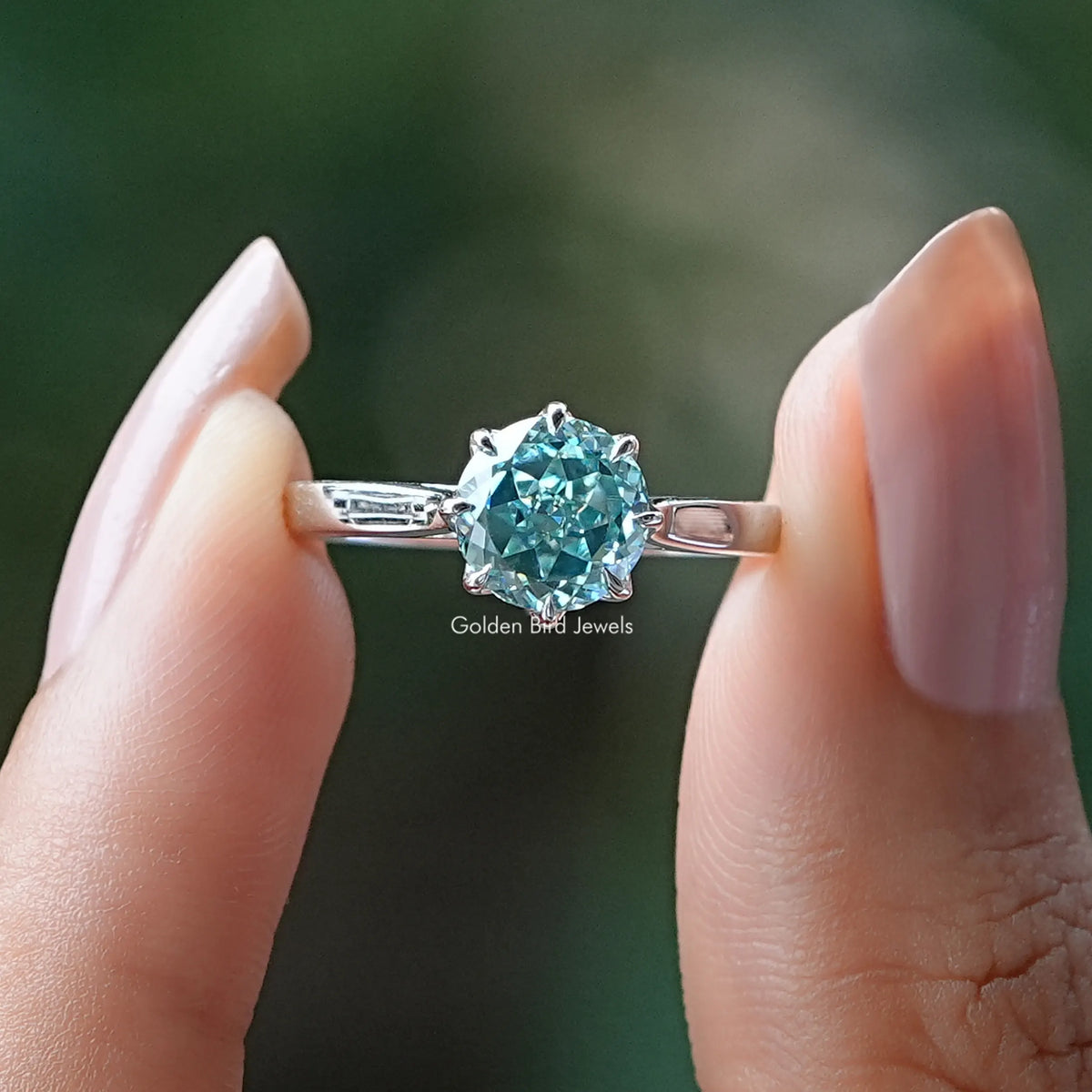 Two fingers holding the Blue Portuguese Round Cut Moissanite Ring