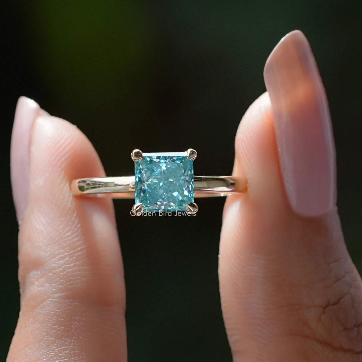 Two fingers holding the Blue Princess Cut Moissanite Ring