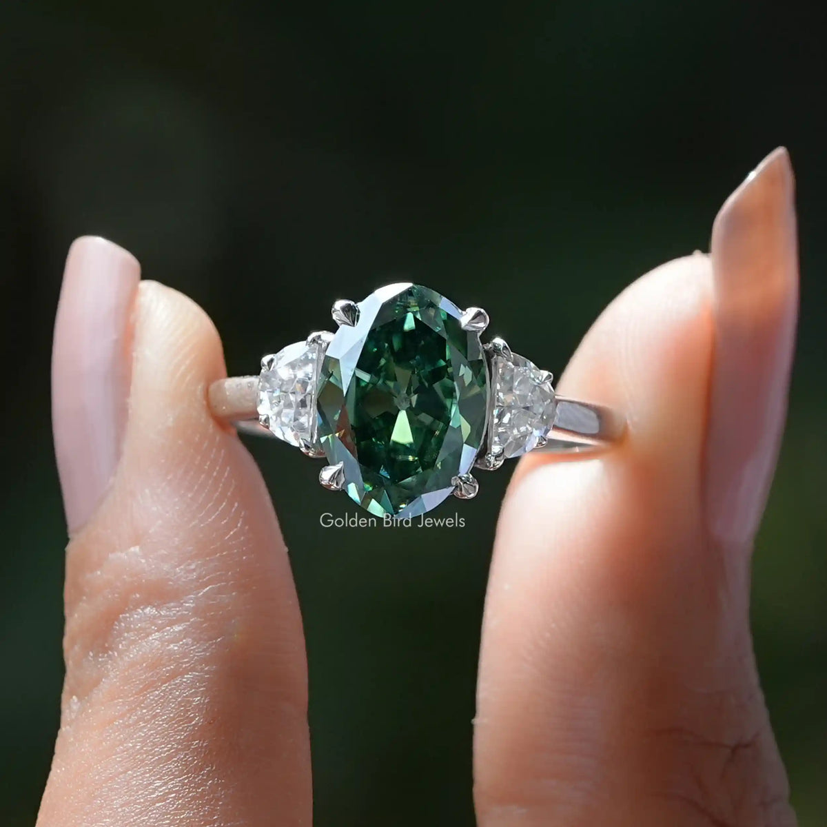 Two fingers holding the Green Oval Cut Moissanite 3 Stone Ring