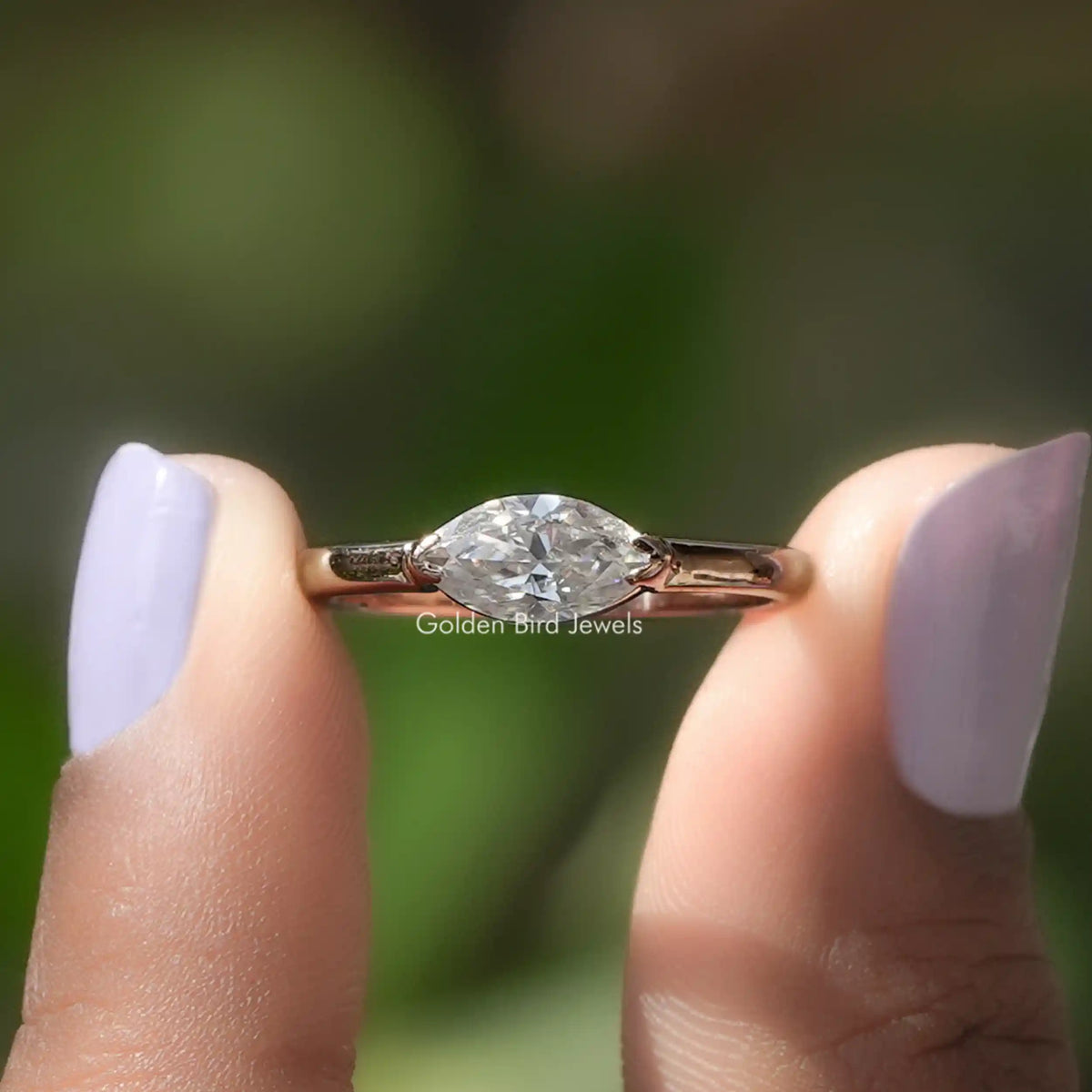 Two fingers holding the East West Marquise Cut Solitaire Ring