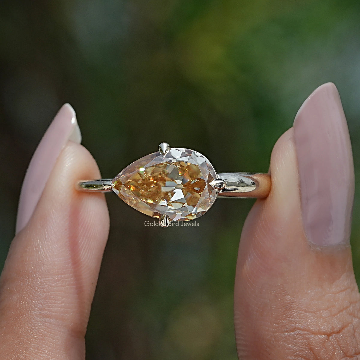 Two fingers holding the Pear Shape Moissanite East West Ring