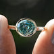 Front view of Blue Green Moissanite Step Cut Oval Solitaire Ring in two fingers 