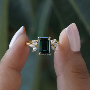 [In two finger front view of emerald cut ring made of dark green stone with side marquise cut stones]-[Golden Bird Jewels]