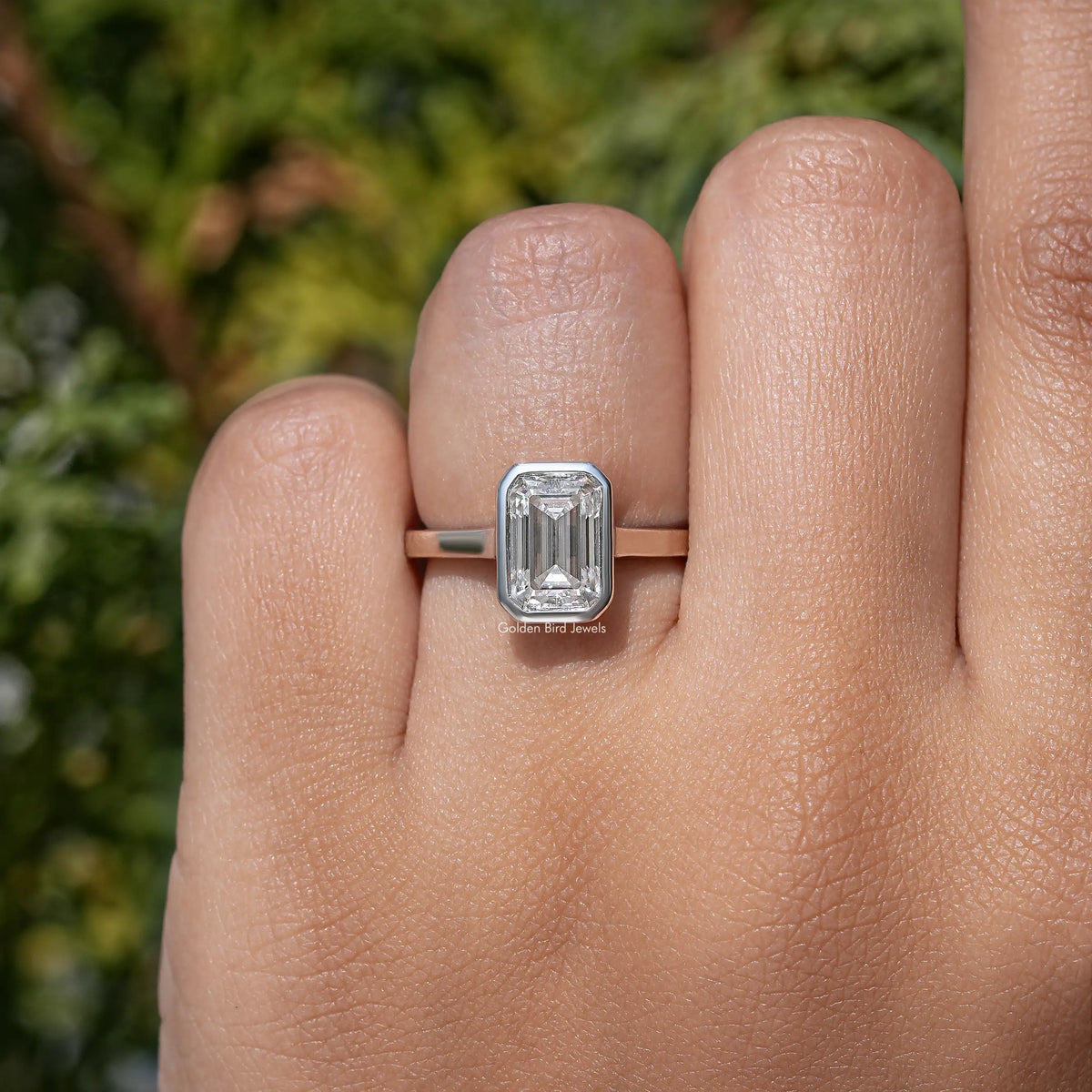 Emerald-cut moissanite bezel-set solitaire ring on finger, square stepped setting