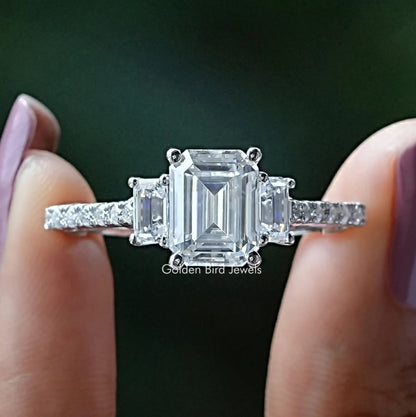 Front View of Emerald Cut Three Stone Moissanite Engagement Ring In two Fingers