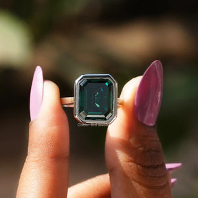 Two fingers holding the Green Emerald Cut Moissanite Solitaire Ring