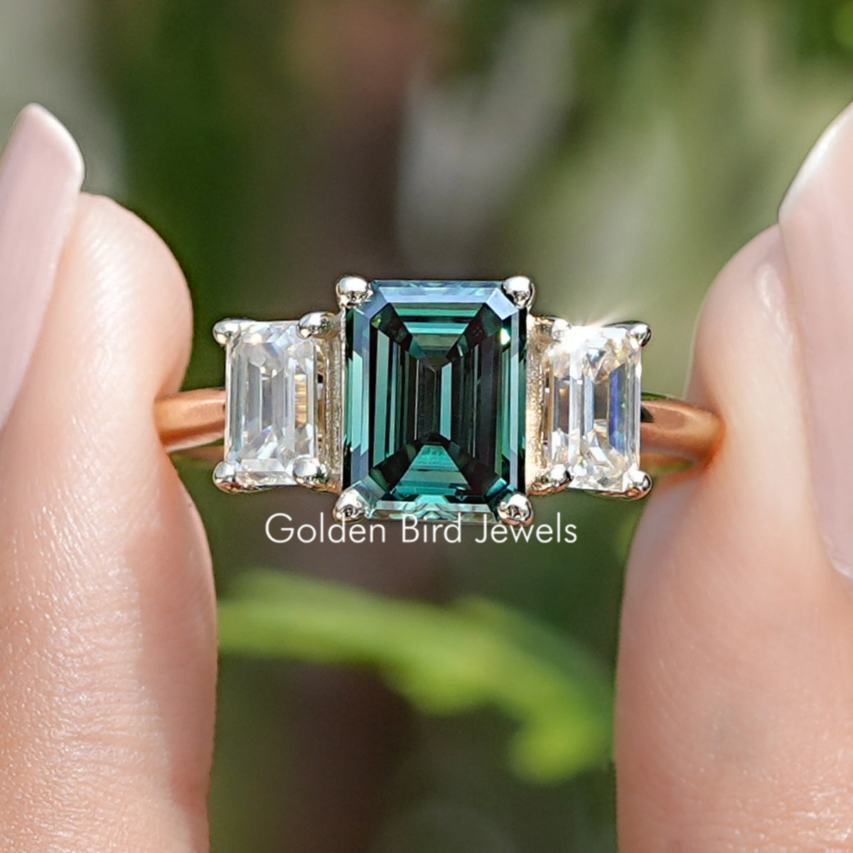Three-stone emerald-cut moissanite ring with a green center and off-white side stones