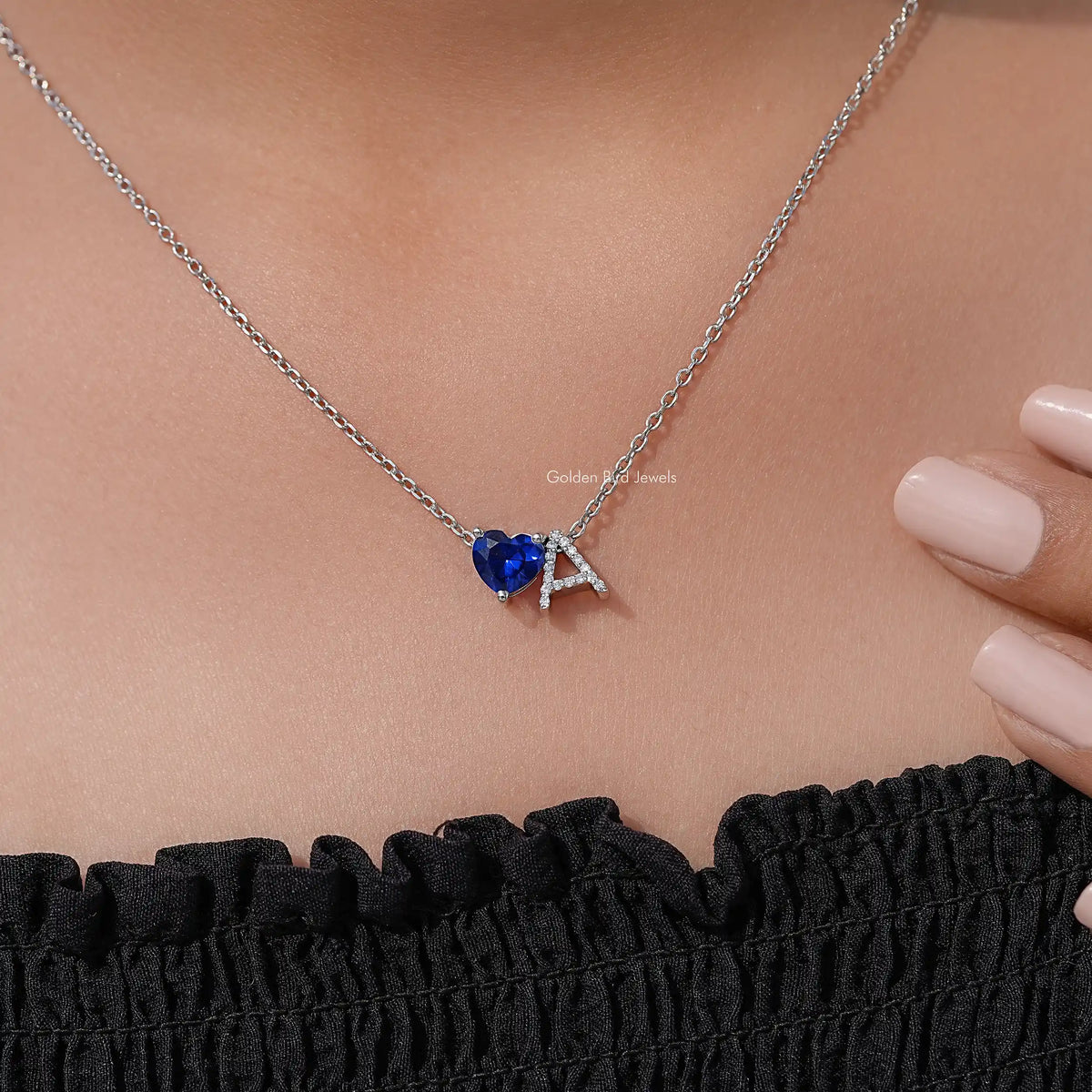 Blue heart gemstone pendant necklace with silver chain and letter A charm, on neckline
