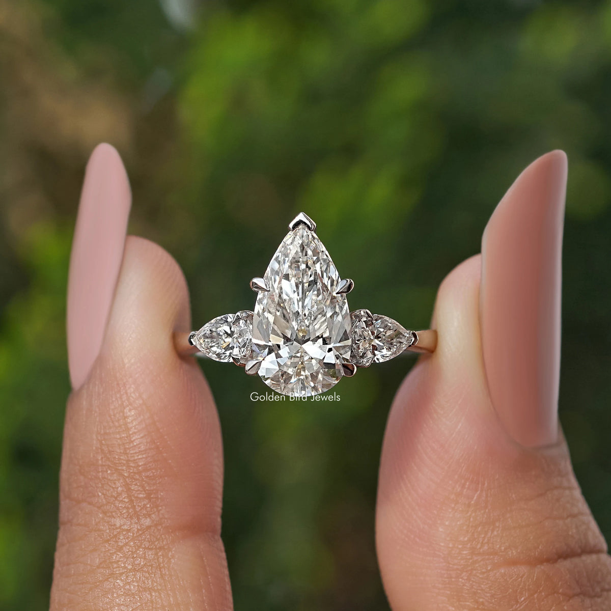 Three Stone Pear Shaped Diamond Engagement Ring Held Between Fingers