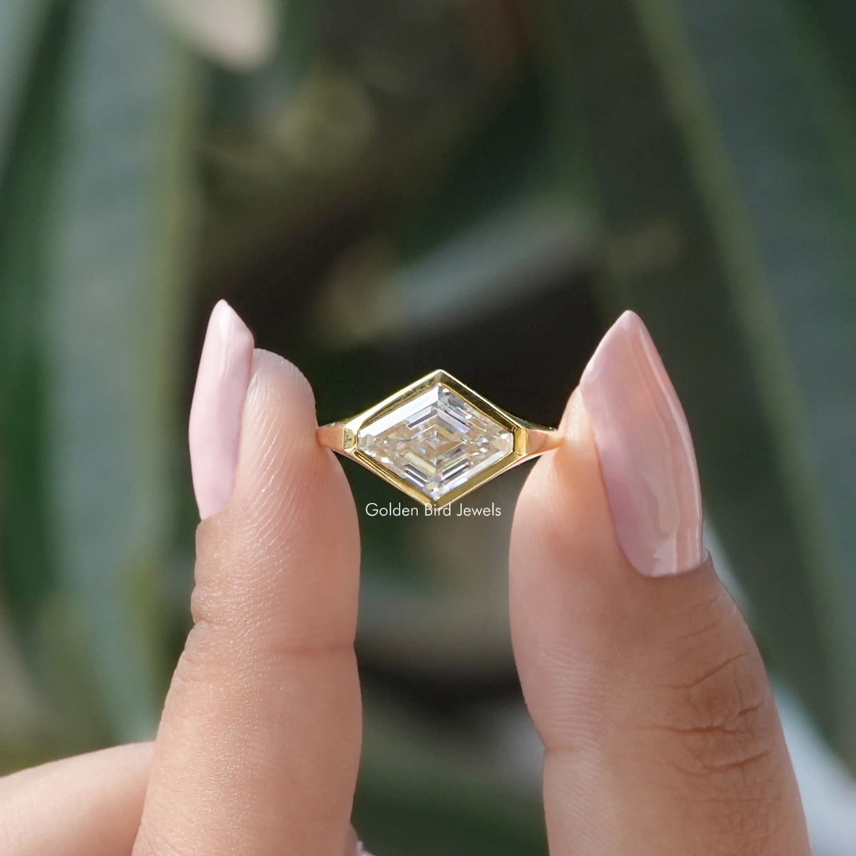 Two fingers holding the Lozenge Cut Moissanite Bezel Set Solitaire Ring