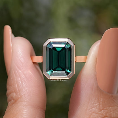 Emerald green moissanite solitaire ring with emerald-cut stone in rose gold-tone setting