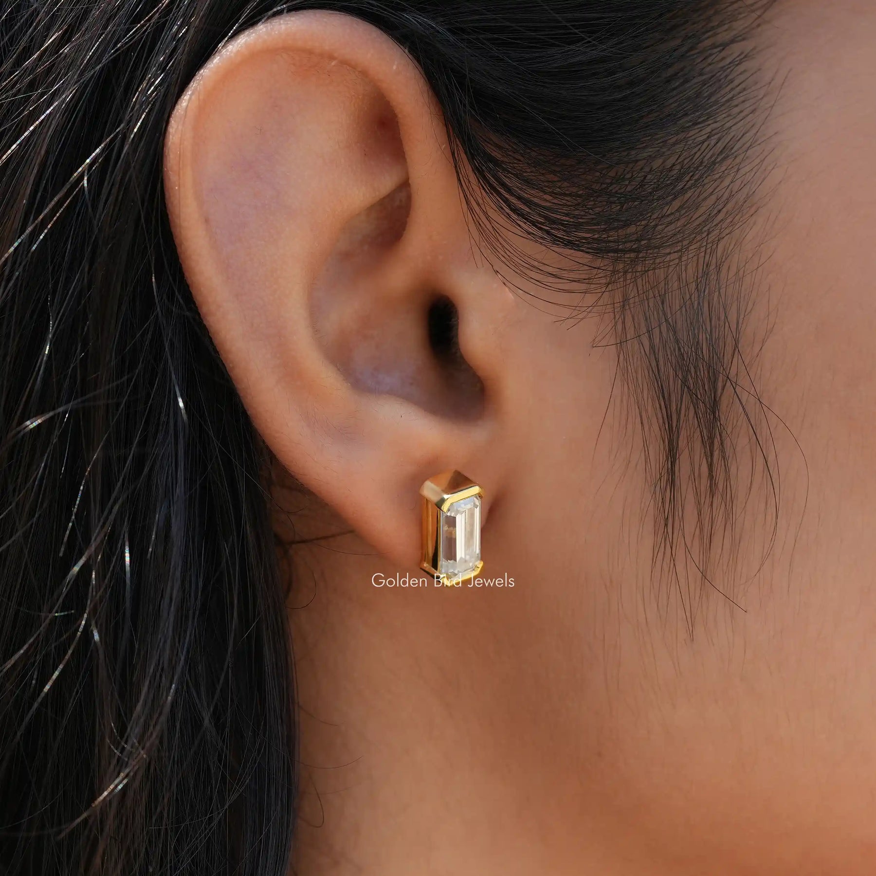[In ear front view of bezel set emerald cut earrings in 14k yellow gold]-[Golden Bird Jewels]