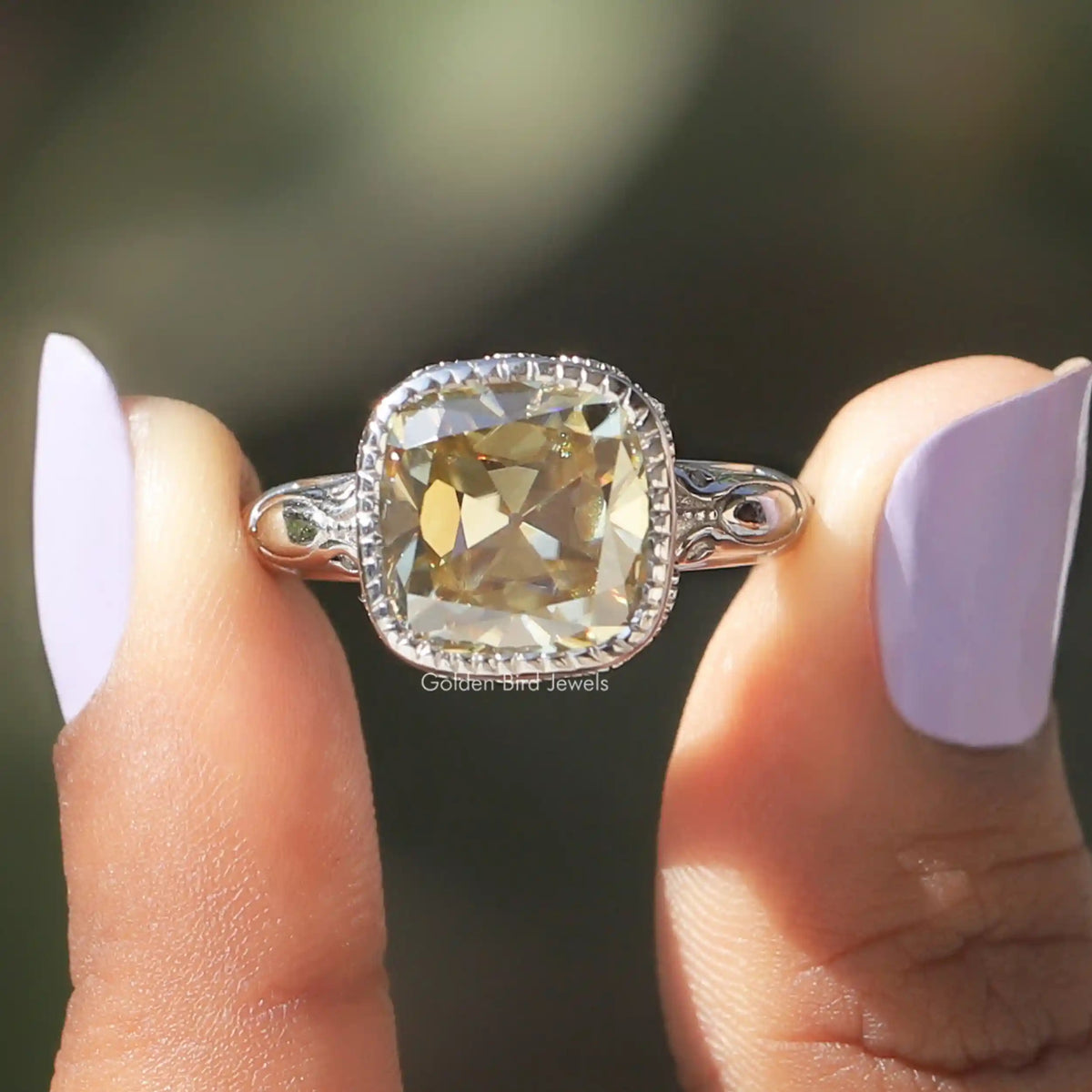 [In two finger front view of moissanite cushion cut engagement ring made of bezel setting]-[Golden Bird Jewels]