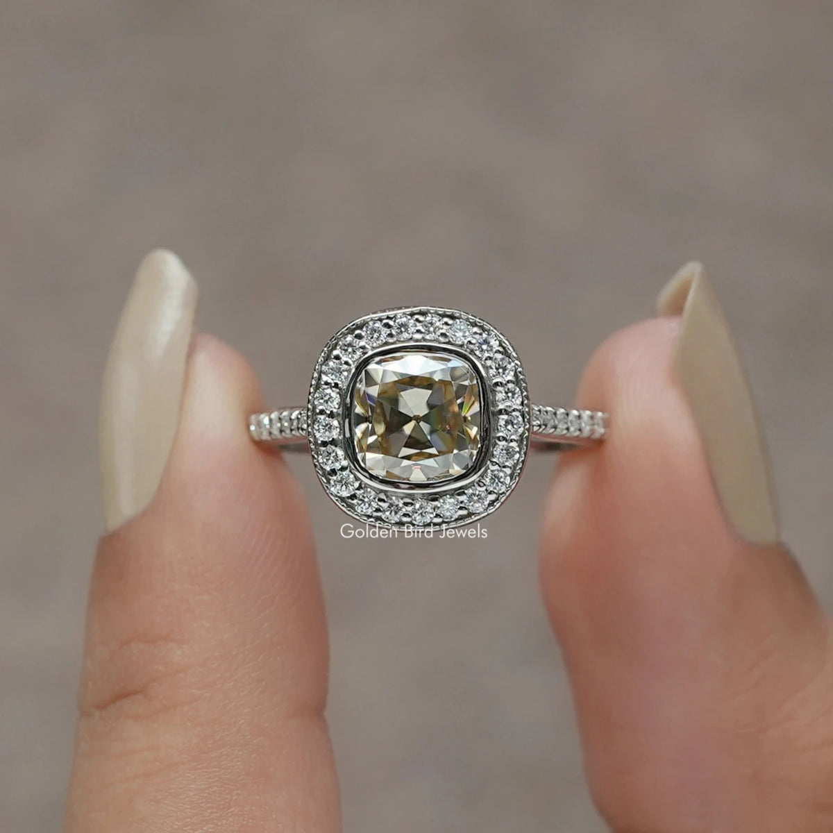 Two fingers holding the Moissanite Old Mine Cushion Cut Halo Ring