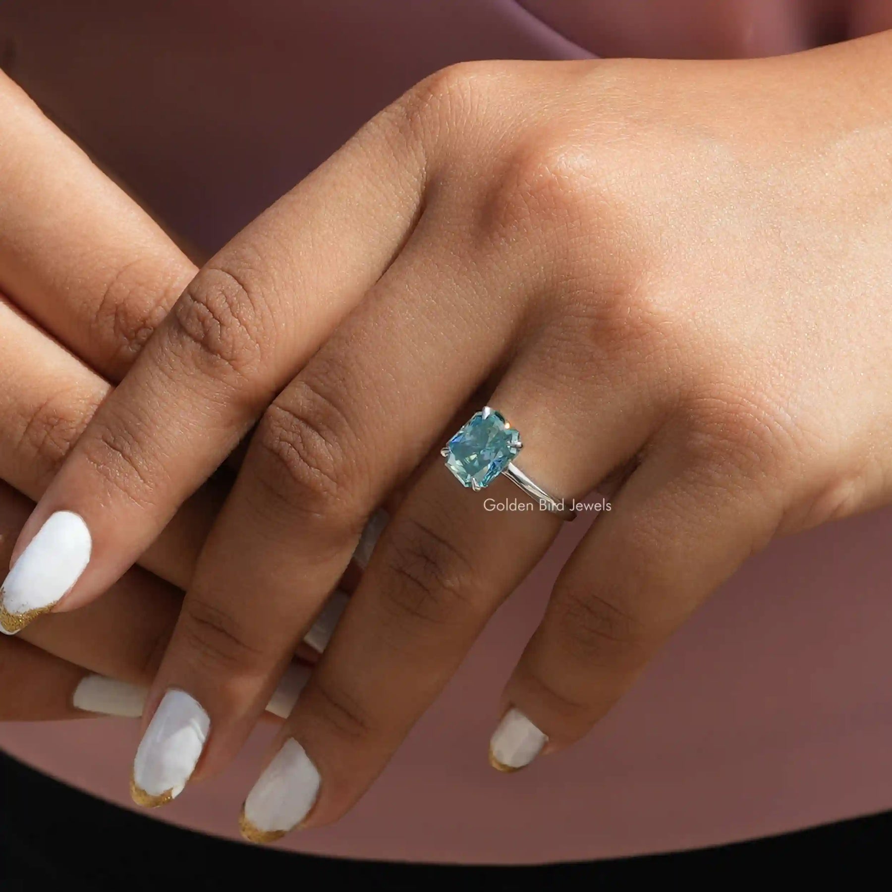 [In fnger front view of blue radiant cut solitaire ring mad of four prongs]-[Golden Bird Jewels]