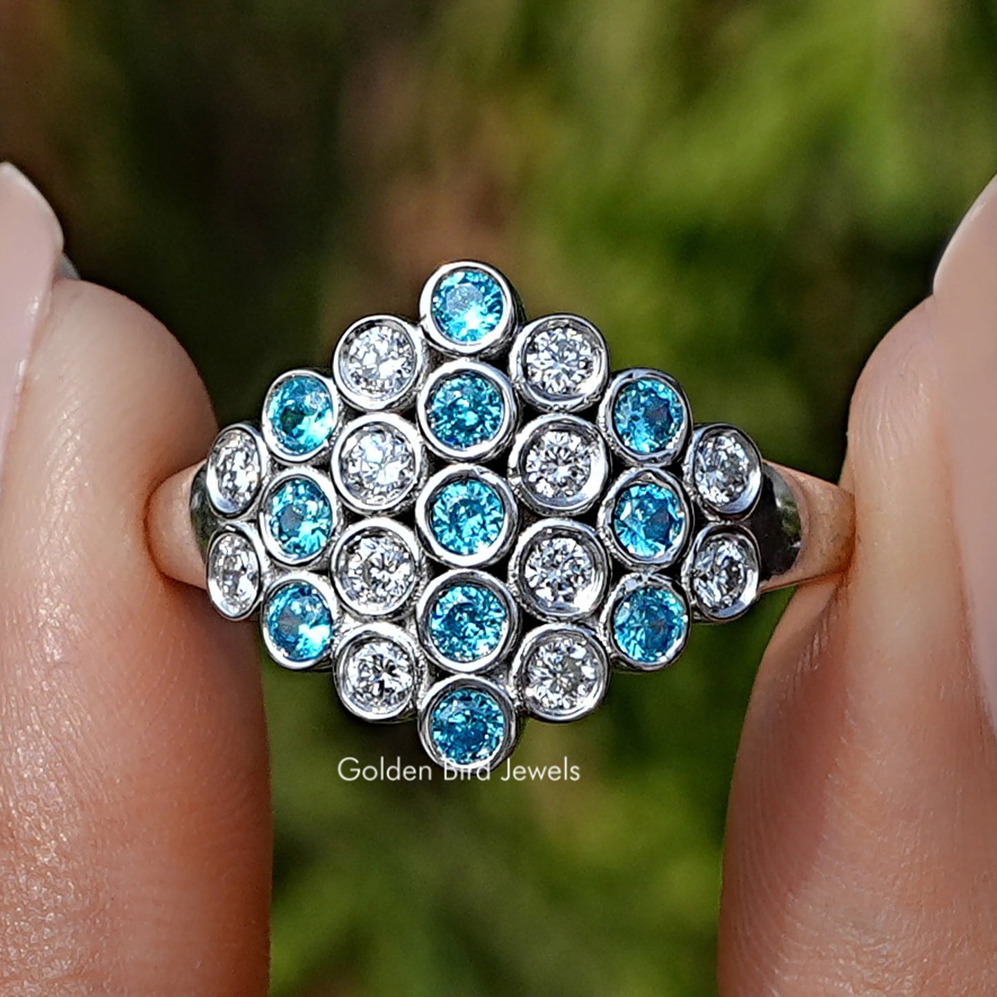Round Cut Paraiba Gemstone Cluster Engagement Ring held between fingers