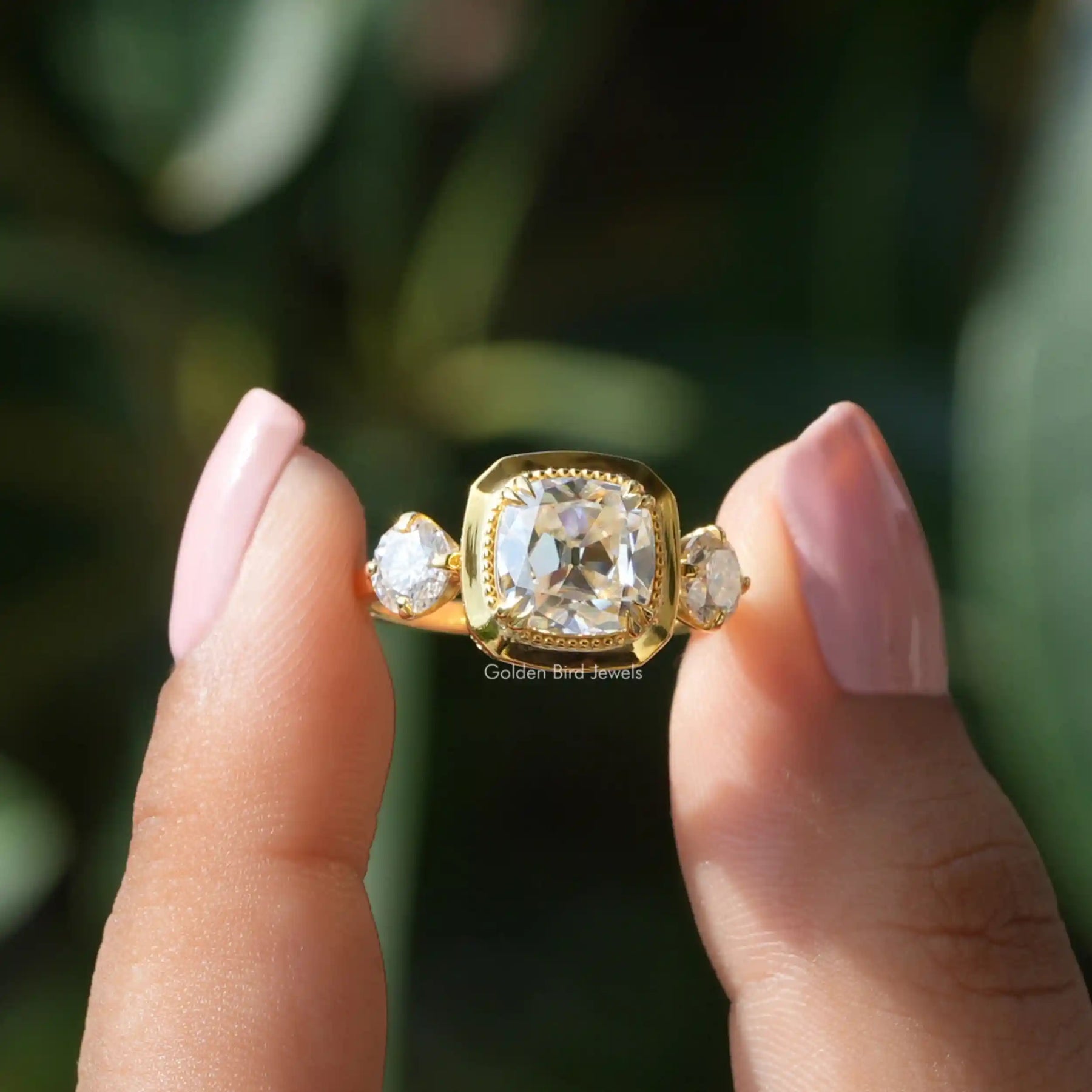 [In two finger front view of old mine cushion cut moissanite engagement ring in 14k yellow gold]-[Golden Bird Jewels]