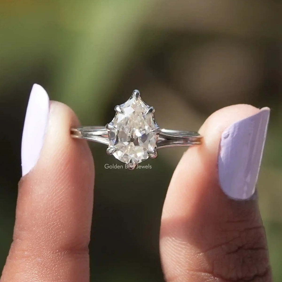Front view of pear cut moissanite  engagement ring holding in two fingers 