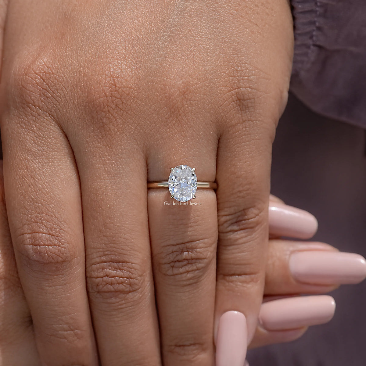 Gold-tone oval moissanite ring on hand with four-prong setting
