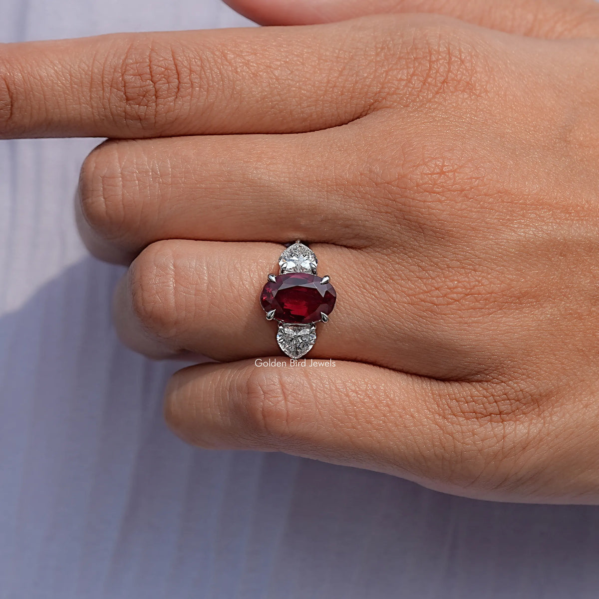 Three-stone oval ruby ring with red center gemstone and white side stones on hand