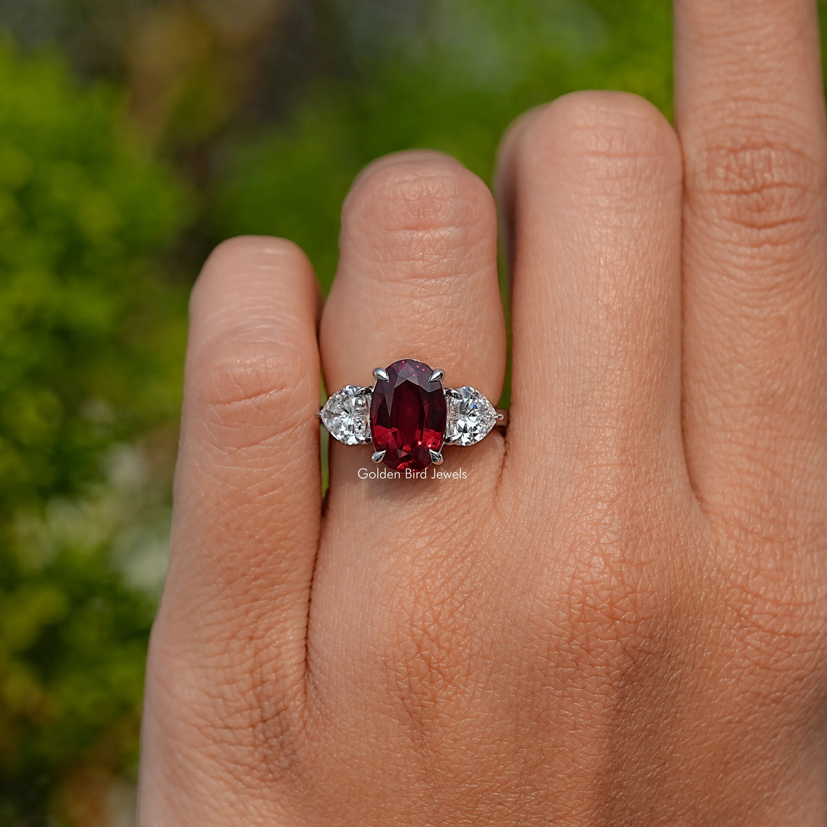 Three-stone ruby ring with oval red center and white side stones, close-up on hand