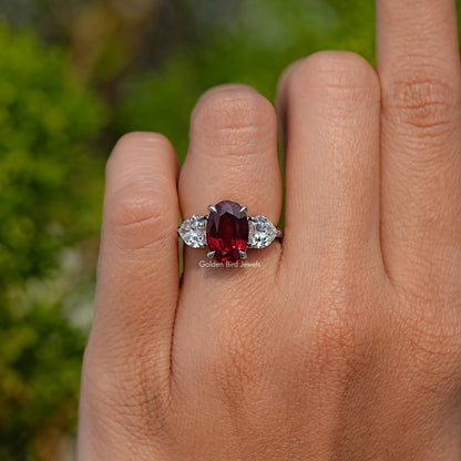 Three-stone ruby ring with oval red center and white side stones, close-up on hand
