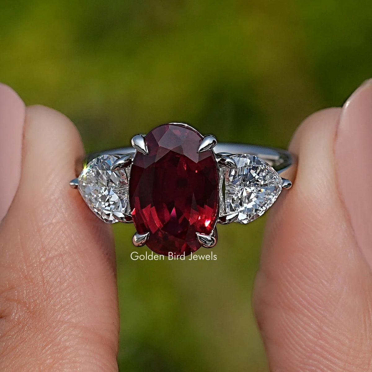 Three-stone ruby ring with oval red center and white side stones in prong setting