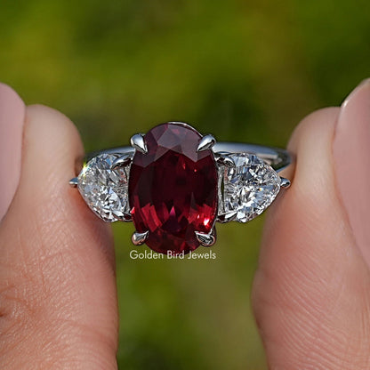 Three-stone ruby ring with oval red center and white side stones in prong setting